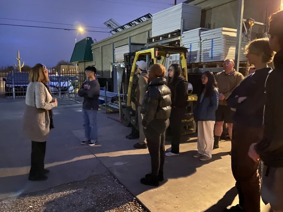 Students listening to speaker in work yard of business